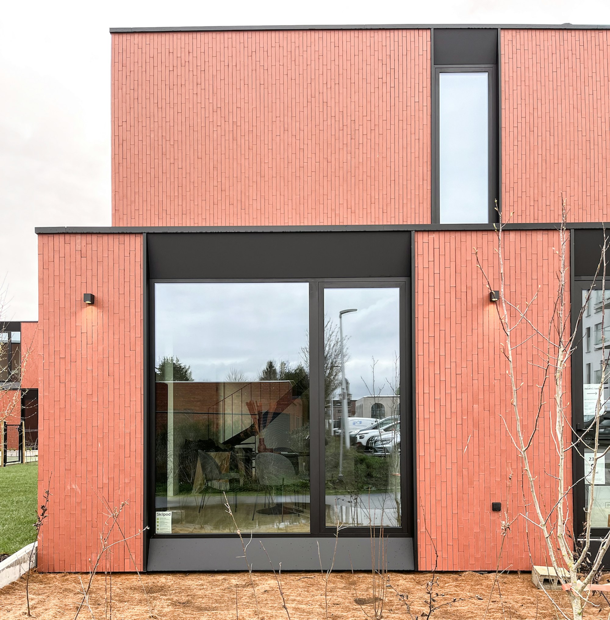 Detail van een #130 Skilpod houtskeletbouw prefab woning met afwerking in rode steen, groot zwart raam